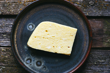 homemade organic yellow cheese with holes in a plate on a dark old table top view