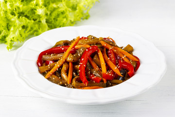 Vegetable salad. Aubergines fried, pepper, carrots on a white plate. The concept of healthy eating. White wooden background. Copy space
