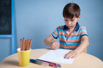 Caucasian boy carefully drawing with colorful pencils.