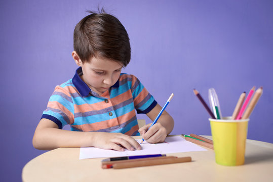 Caucasian boy carefully drawing with colorful pencils.