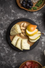 Closeup view of caciotta cheese with almond, pears on wooden plate on dark background