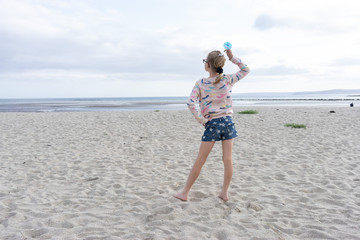 Female child posing on the beach with a cocktail umbrella from behind 