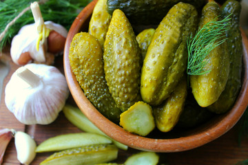 Cucumbers in a wooden bowl, fresh herbs, pickling spices and jars of pickled cucumbers on the table