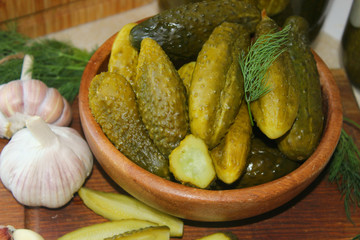 Cucumbers in a wooden bowl, fresh herbs, pickling spices and jars of pickled cucumbers on the table