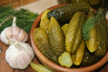 Cucumbers in a wooden bowl, fresh herbs, pickling spices and jars of pickled cucumbers on the table