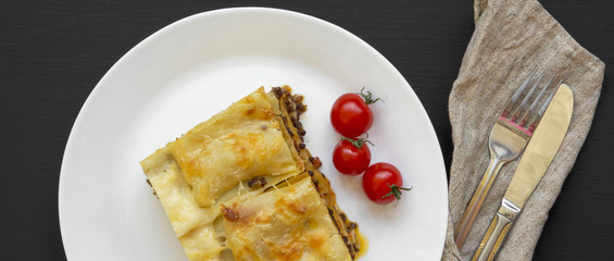 Traditional beef lasagna on a white round plate on black background, overhead view. Close-up.
