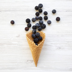 Waffle sweet ice cream cone with blueberries on a white wooden table, top view. From above, overhead, flat lay.