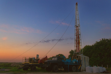 drilling rig drills a well for the extraction of drinking water at sunset under a beautiful sky for drinking people