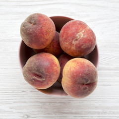 Pink bowl of fresh peaches on white wooden surface, overhead view. From above, top view. Close-up.