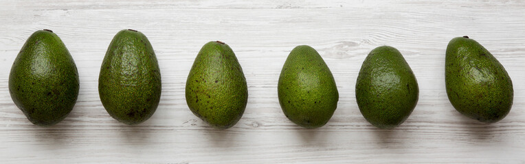 Whole avocados on white wooden background, overhead view. Flat lay, from above. Close-up.