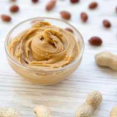 Bowl of peanut butter with peanuts over white wooden table, side view. Closeup.