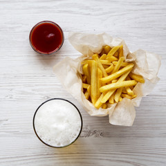French fries with sauce and cold beer on a white wooden table, overhead view. From above, top view.