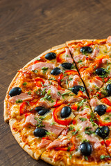 slices of Pizza with Mozzarella cheese, ham, pepper, meat, Tomatoes, olives, Spices and Fresh Basil. Italian pizza on wooden background