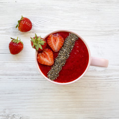 A cup of strawberry smoothie with chia seeds on a white wooden background, overhead view. Close-up.