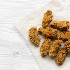 Fried chicken wings on baking paper sheet on a white wooden table, overhead. From above, flat lay, top view.