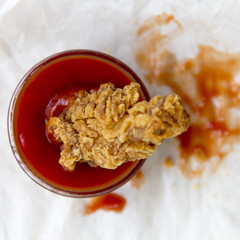 Fried chicken wing in a bowl of sauce, overhead view. From above. Close-up.