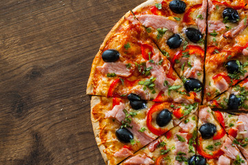 slices of Pizza with Mozzarella cheese, ham, pepper, meat, Tomatoes, olives, Spices and Fresh Basil. Italian pizza on wooden background