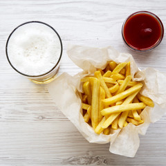 French fries with sauce and cold beer on a white wooden background, top view. From above, overhead. Close-up.