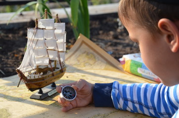 Boy in the image traveler studying his map of travel and adventure in nature. old ship sailboat on an old vintage map, an infamous pipe, a Columbus day concept. sailor