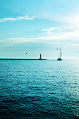 Yacht on the background of a lighthouse and sea horizon with a cold-filter.
