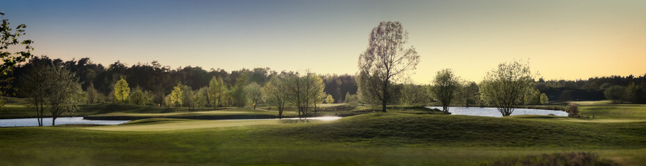 Fototapeta na wymiar Panorama von einem Golfplatz mit Bäumen Büschen und Teichen im Sonnenuntergang