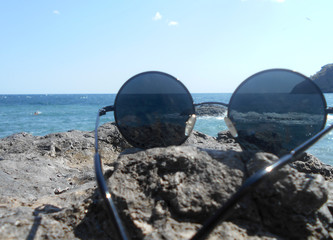 Fototapeta na wymiar fashionable round sunglasses lie on the rocks of the blue sea in summer