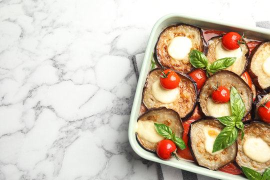 Baked eggplant with tomatoes, cheese and basil in dishware on marble table, top view. Space for text