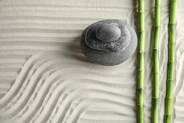 Fototapeta premium Bamboo branches with spa stones on sand, top view. Space for text