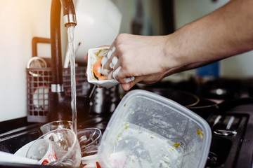 The man cleans the cup after coffee with a scourer. Dirty dishes in the sink. No dishwasher. Concept of caring for dishes in the kitchen. The kitchen sink is full of dirty dishes.