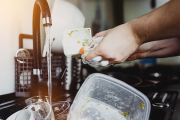 The man cleans the cup after coffee with a scourer. Dirty dishes in the sink. No dishwasher. Concept of caring for dishes in the kitchen. The kitchen sink is full of dirty dishes.