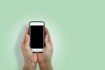 Two hands are holding a white cell phone with a blank black display. Content completion concept. Hands are holding a smartphone from below, front view on a pastel green background.