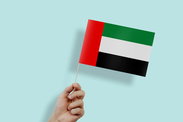 UAE flag held in the hands. The hand raises the flag of United Arab Emirates on a green, pastel background. The concept of citizens, independence, love for their country. Patriotism.