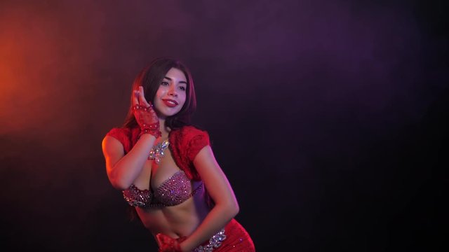 Tempting sexy traditional oriental belly dancer girl dancing on purple neon smoke background. Woman in exotic red costume sexually moves her semi-nude body. 4k
