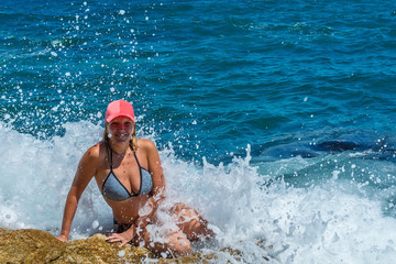 A beautiful girl poses on a rock and enjoys in waves