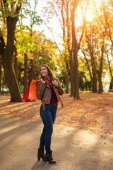 Fototapeta premium Beautiful young woman happy after shopping and walking in a park in autumn
