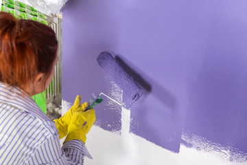 woman paints white wall and purple paint with roller