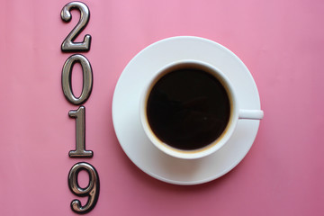 The new year is 2019. Classic American coffee in a small white ceramic Cup on a pink bright top view background. Copy space, space for writing texts. 