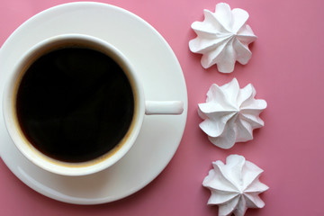Classic American coffee in a small white ceramic Cup on a pink bright background and white cakes, meringue. The view from the top. Copy space, space for writing texts.