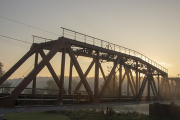 Fototapeta na wymiar A railway bridge in the morning fog or smoke through which the rays of the sun shine