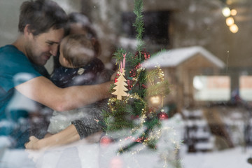 Young couple with a baby standing next to a decorated Christmas tree