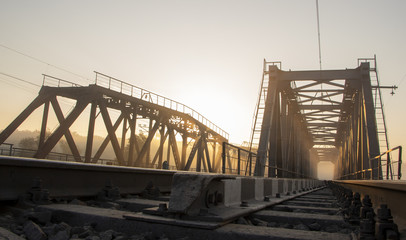 A railway bridge in the morning fog or smoke through which the rays of the sun shine