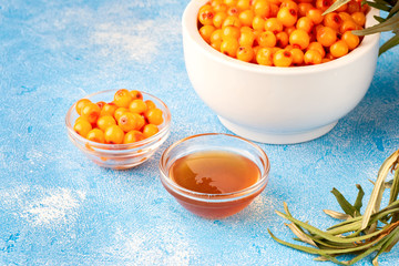 Sea-buckthorn berries in bowl and natural honey or sea buckthorn oil on blue background