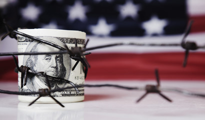 US Dollar money wrapped in barbed wire on United States national flag background as symbol of...