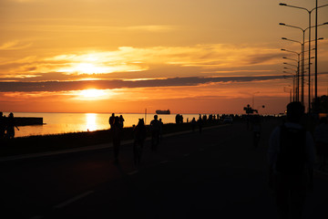 Sunset on the seaside promenade. Silhouettes of people walking on the road