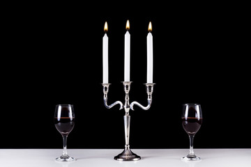 Stylish silver baroque candlestick and two red wine glasses on white desk and black background. Romantic diner concept