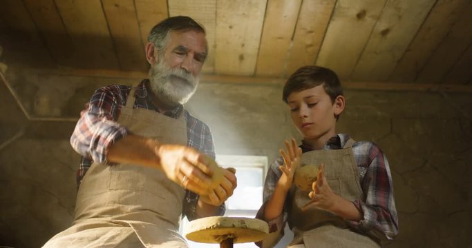 Caucasian grandfather and grandson molding clay in hands and warming it before start sculptoring.