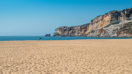 Empty beach with sole parasol next to massive cliff at Nazare, Portugal