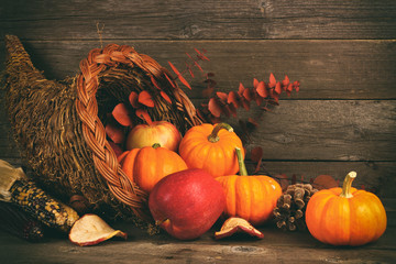 Thanksgiving cornucopia filled with pumpkins and apples against a rustic wooden background