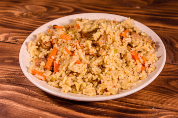 Ceramic plate with pilaf on wooden table