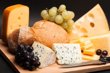 Knife, Cheese, Rolls and Grape on the Wooden Platter on Black